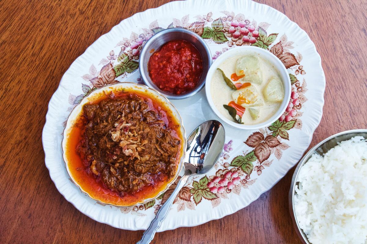An overhead photo of a bowl of beef rendang with crispy shallots on a porcelain platter with chile