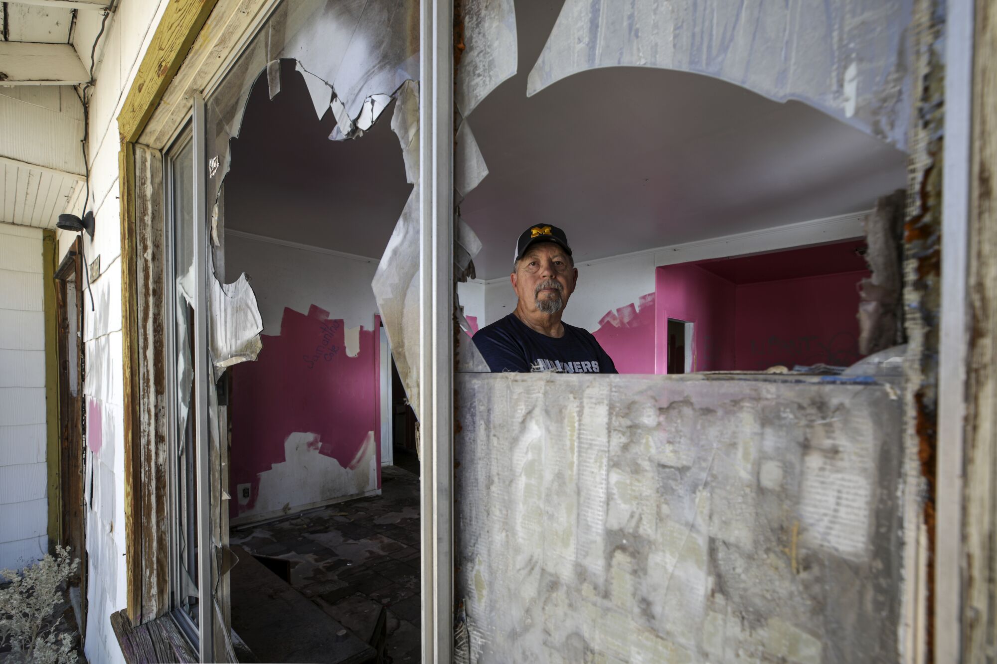 A man stands inside an abandoned home with shattered windows