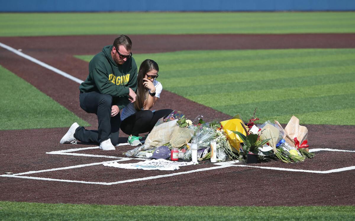 Two people pay their respects at a memorial at home plate in honor of Orange Coast College head baseball coach John Altobelli, who died with his wife, Keri, and daughter Alyssa in Sunday's helicopter crash in Calabasas that also killed Lakers great Kobe Bryant, his daughter Gianna and four others.