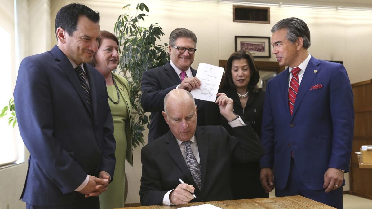 Gov. Jerry Brown hands a copy of a bail bill he signed to state Sen. Bob Hertzberg, along with Assemblyman Rob Bonta, right. Also seen are Assembly Speaker Anthony Rendon, left, Senate President Pro Tem Toni Atkins, left, and state Supreme Court Chief Justice Tani Cantil-Sakauye.