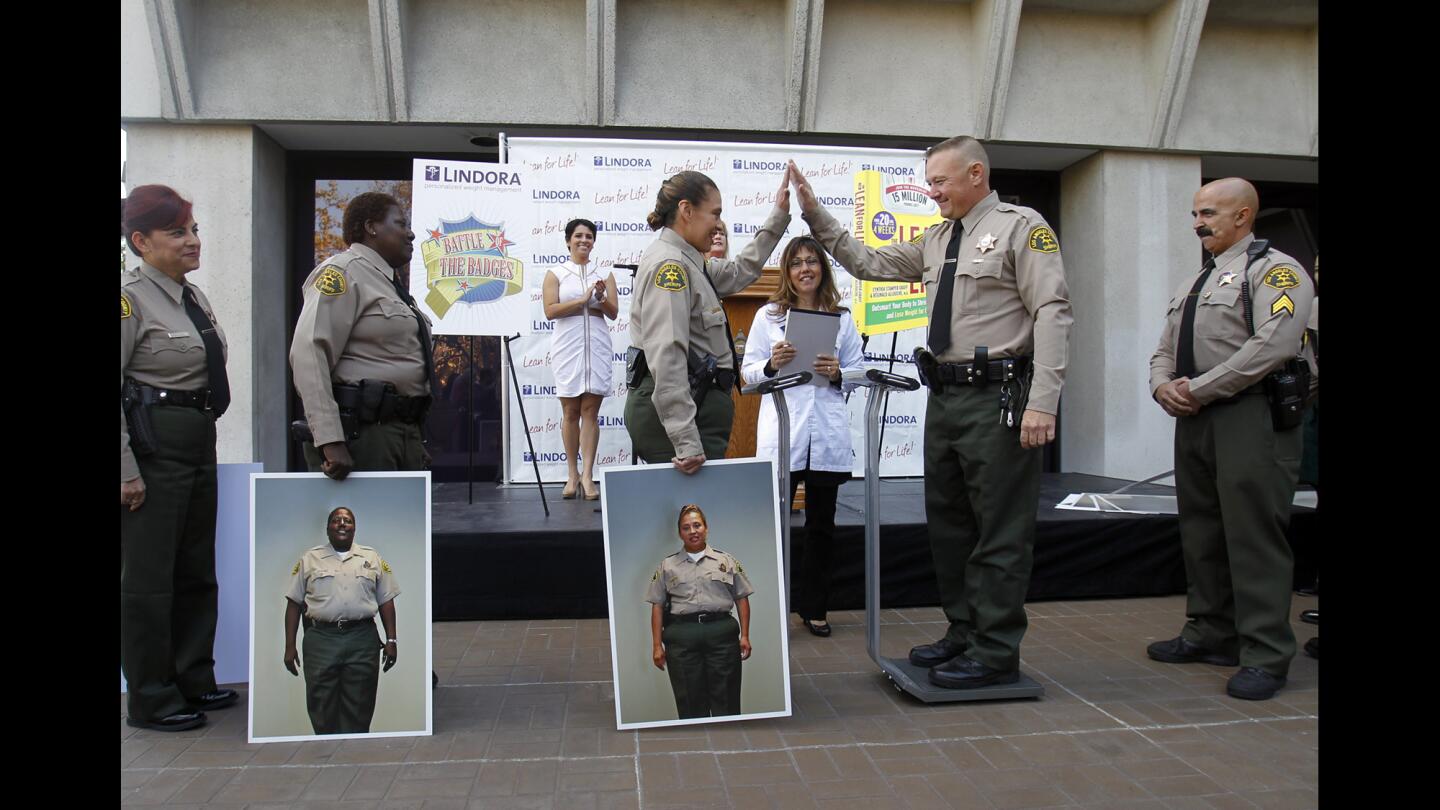 Los Angeles County Sheriff's Deputy Pearl Cruz, center, holding a portrait of herself before she lost 36 pounds, congratulates Deputy Sheriff Brian Knott for his weight loss during a ceremony at sheriff's headquarters in Monterey Park.