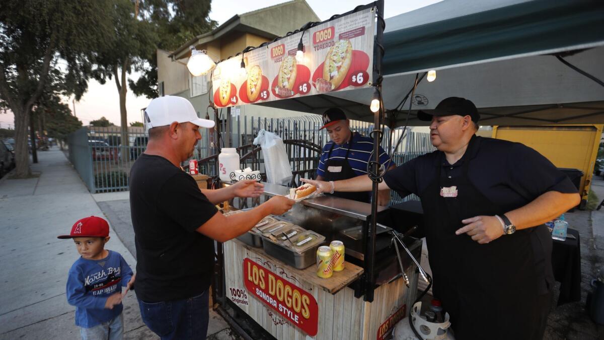 Alejandro Zamorano and his nephew David Zamorano serve Sonoran-style hot dogs at their cart in front of a friend's house in Compton