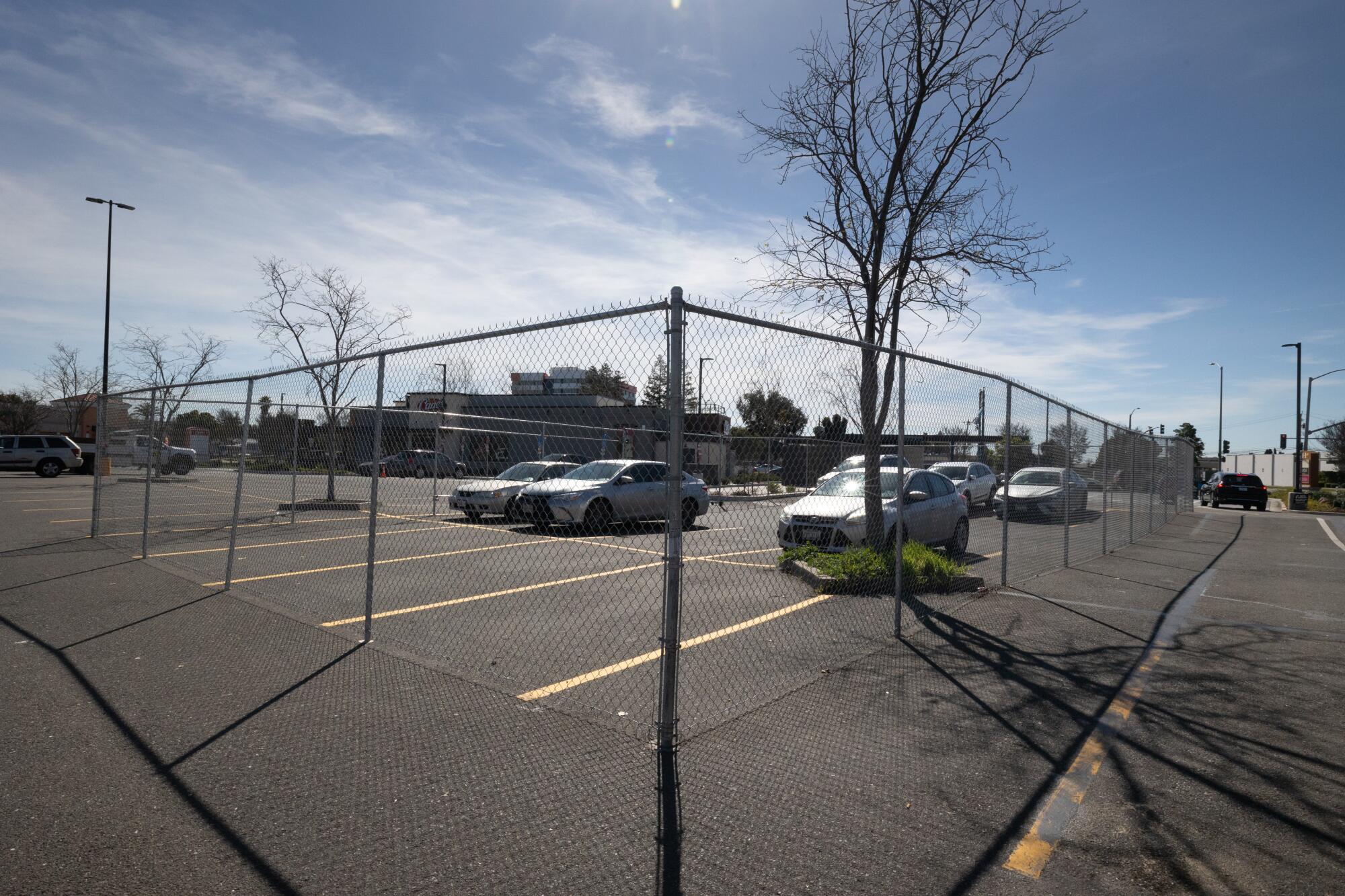 Tall chain-link fencing surrounds part of a parking lot with several cars and additional empty parking spaces