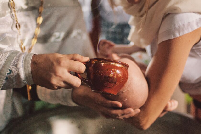 A stock image of a priest baptizing an infant.