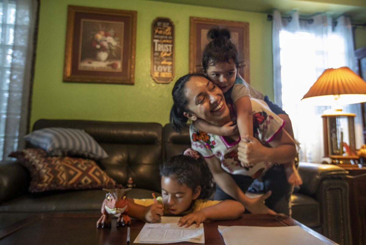 Mireya Tecpaxohitl Gonzalez, 32, carries her son as her daughter, a first-grader, does math homework.