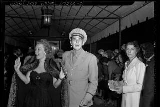 Jane Wyman, wearing a fur coat, gestures with her hands while with Ronald Reagan, who looks toward the photographer