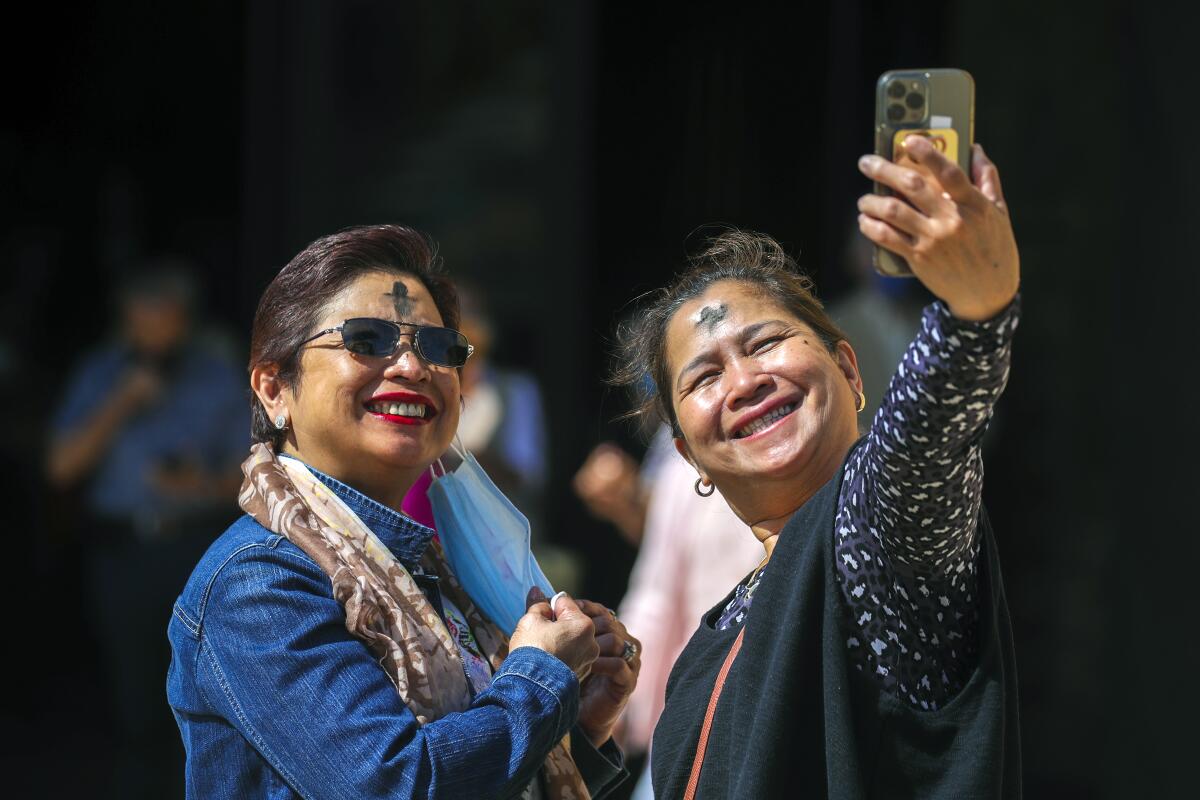 Two women with ash on their foreheads smile for a selfie.
