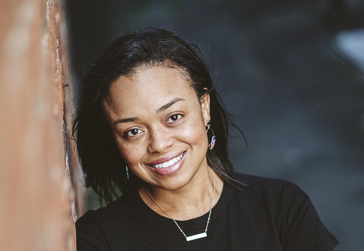 A headshot of a woman smiling and leaning against a wall to her right