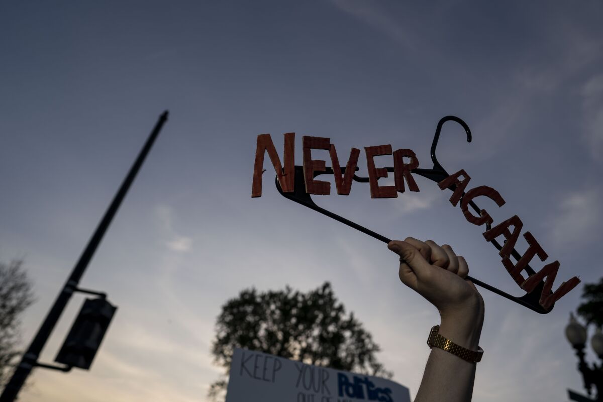 A hand holds up a hanger with the words "Never Again" glued to it, at an abortion rights demonstration  on May 3