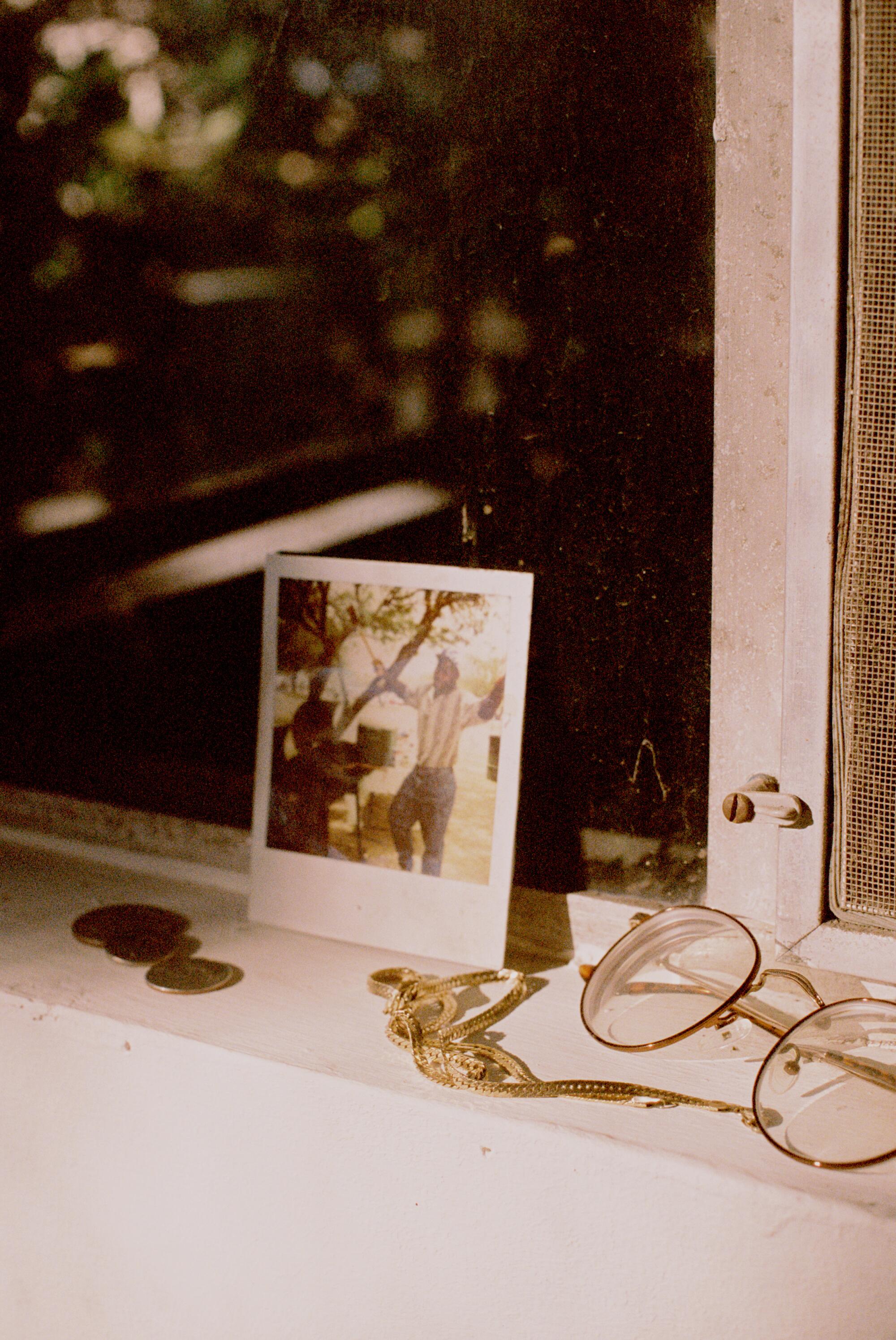 A Polaroid photo and wire-rimmed spectacles on a windowsill