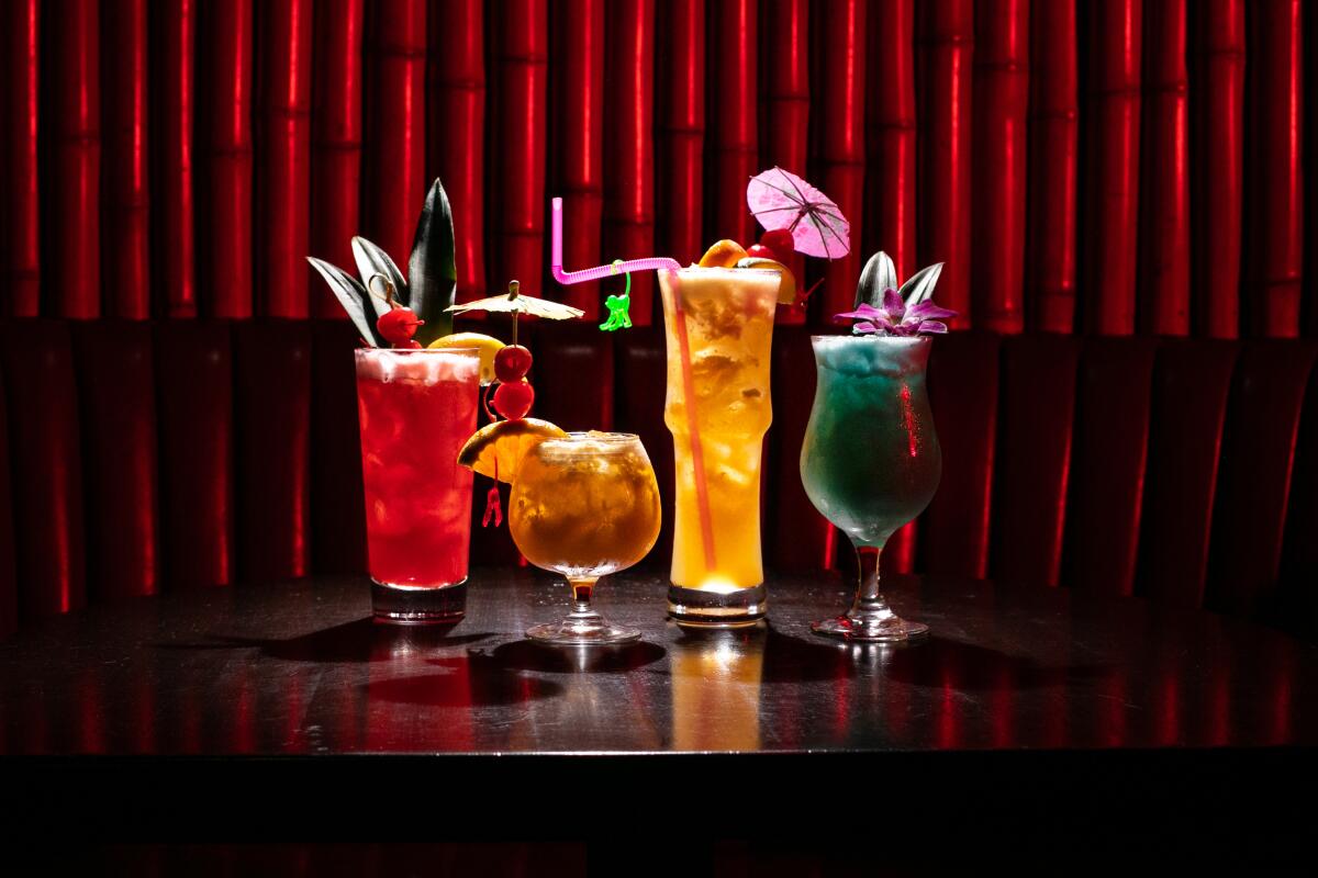 Four glasses with red-, amber-, orange- and blue-colored drinks on a table