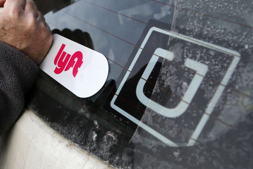 FILE- In this Jan. 31, 2018, file photo, a Lyft logo is installed on a Lyft driver's car next to an Uber sticker in Pittsburgh. Lyft and Uber are expanding deeper into health care by offering to take more patients to and from non-emergency medical appointments in markets around the country. (AP Photo/Gene J. Puskar, File)
