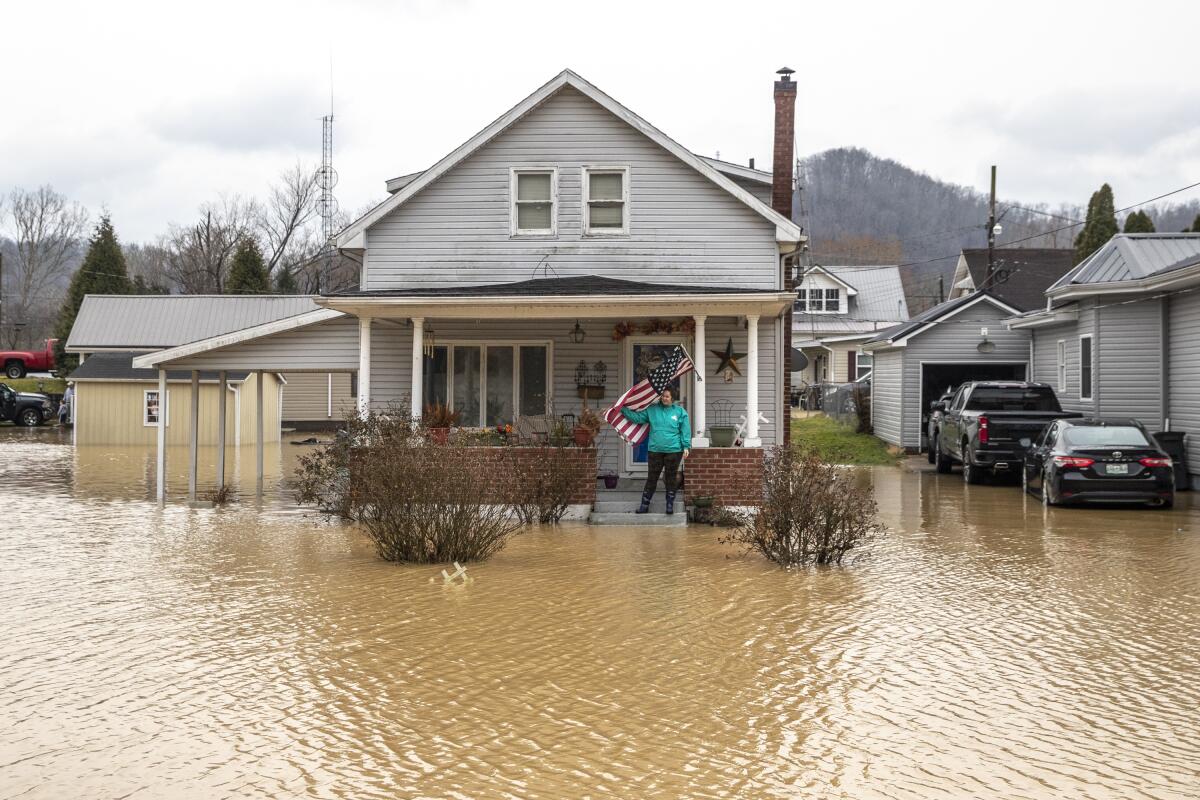 A woman stands on the porch of her home in Paintsville, Ky., as floodwaters approach