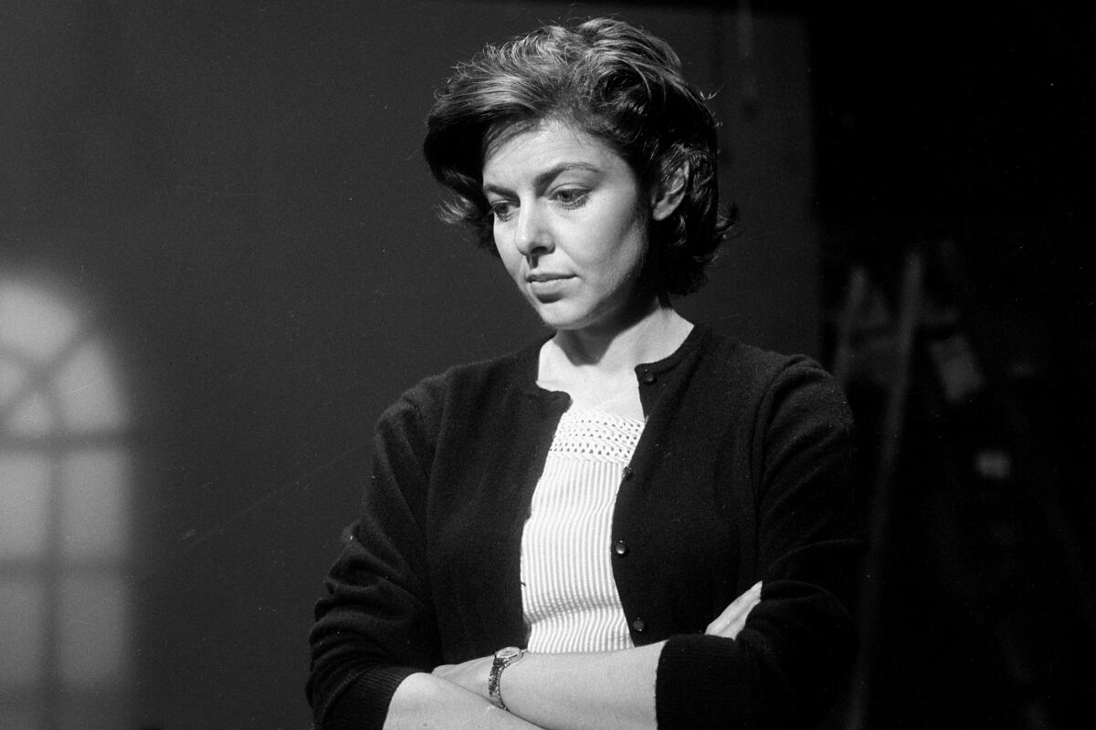 A black-and-white photo of Elaine May looking down with her arms folded.