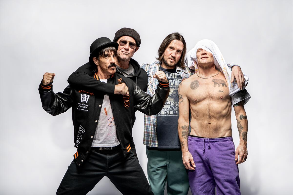 Group photo of Red Hot Chili Peppers. Bare-chested Flea has a T-shirt draped halfway across his face.
