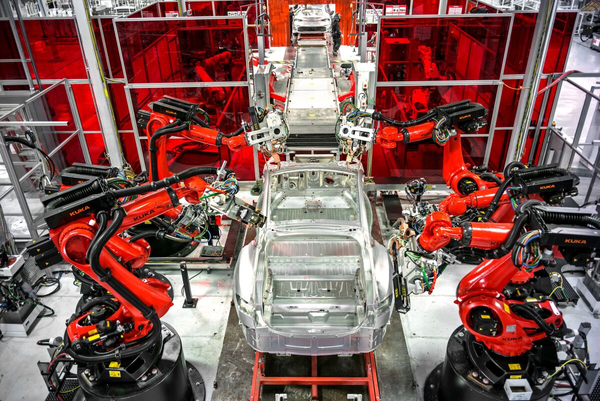 Robots assemble parts of a car at the Tesla factory.