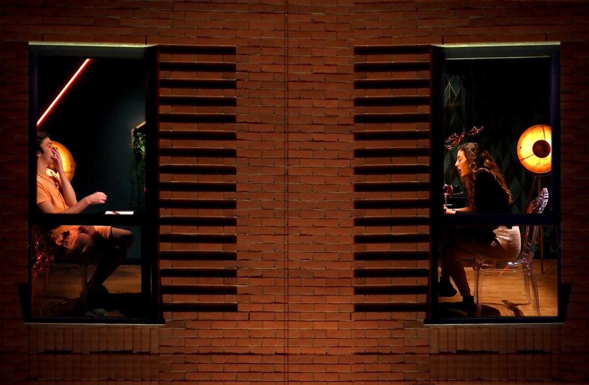 A man and a woman in separate apartments, pictured through their windows