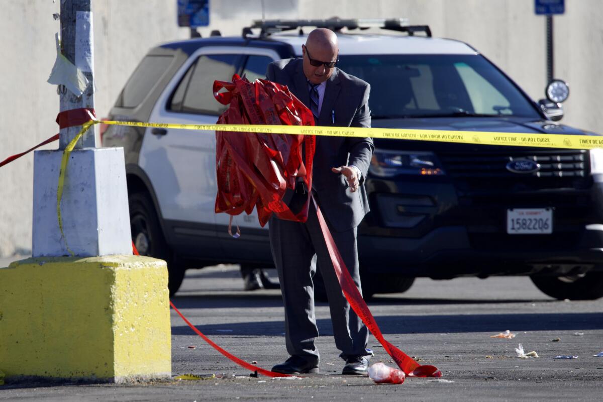 A police investigators carries crime scene tape while standing in front of a patrol cruiser in a parking lot