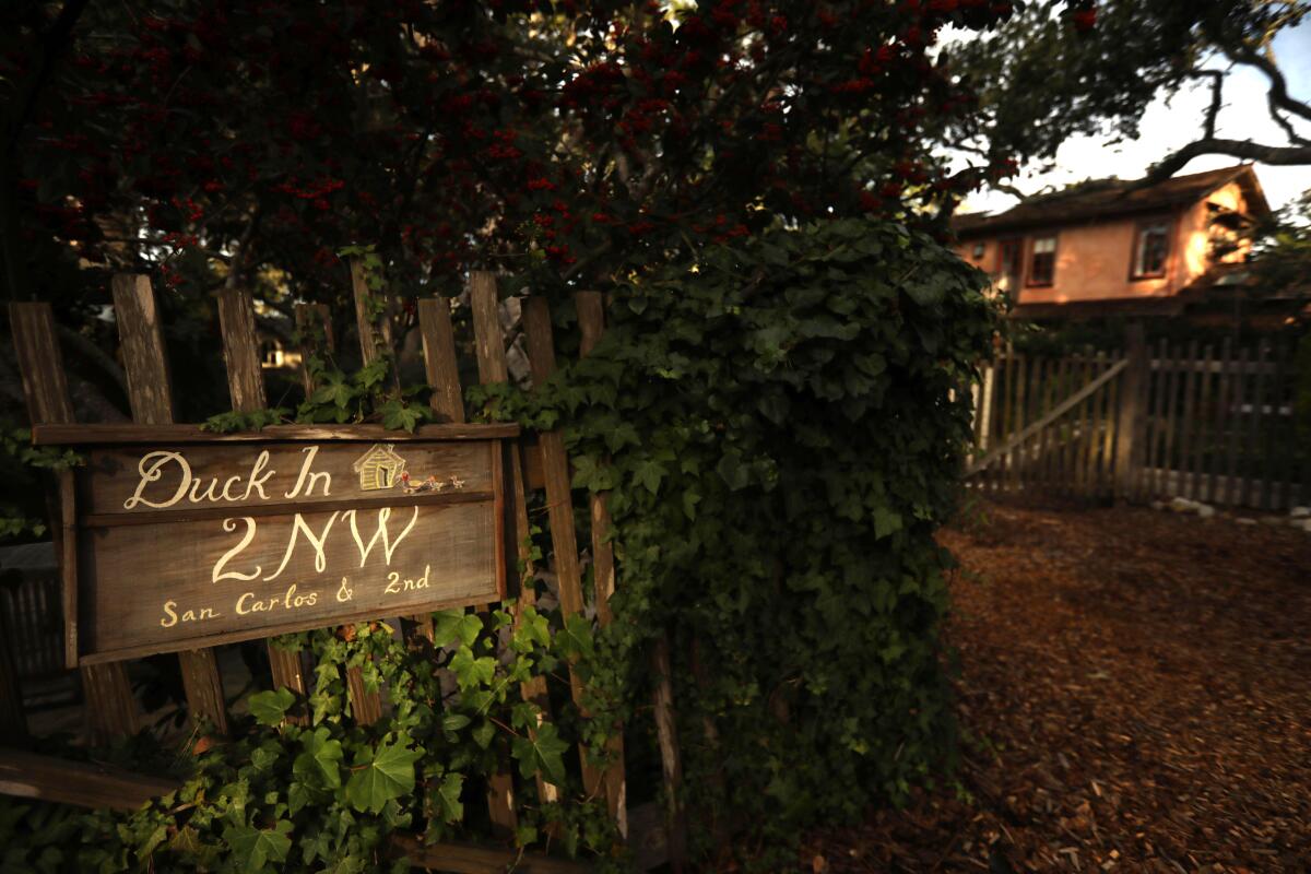 A painted wooden sign with the name and address of a house, on a fence outside the house