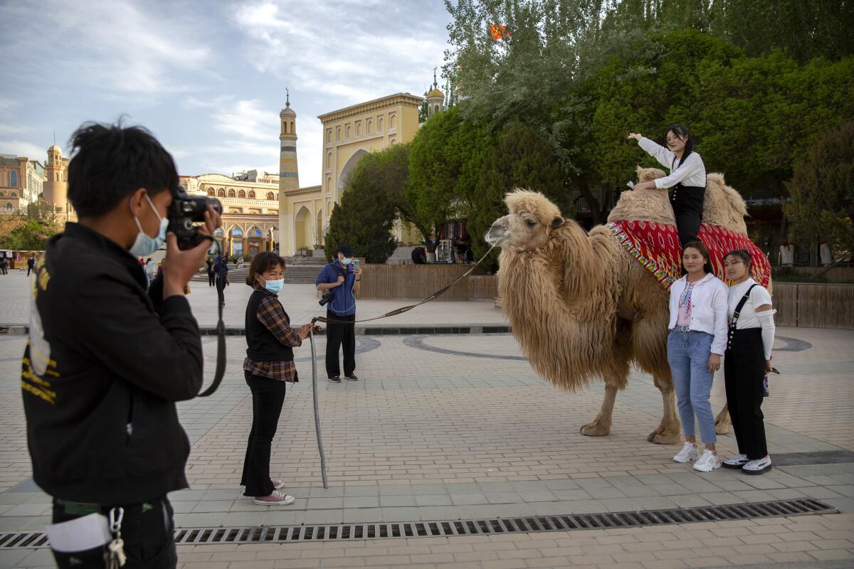FILE - Tourists pose for photos with a camel outside the Id Kah Mosque in Kashgar in western China's Xinjiang Uyghur Autonomous Region, as seen during a government organized trip for foreign journalists, on April 19, 2021. After a U.N. report concluding that China's crackdown in the far west Xinjiang region may constitute crimes against humanity, China used a well-worn tactic to deflect criticism: blame a Western conspiracy. (AP Photo/Mark Schiefelbein, File)