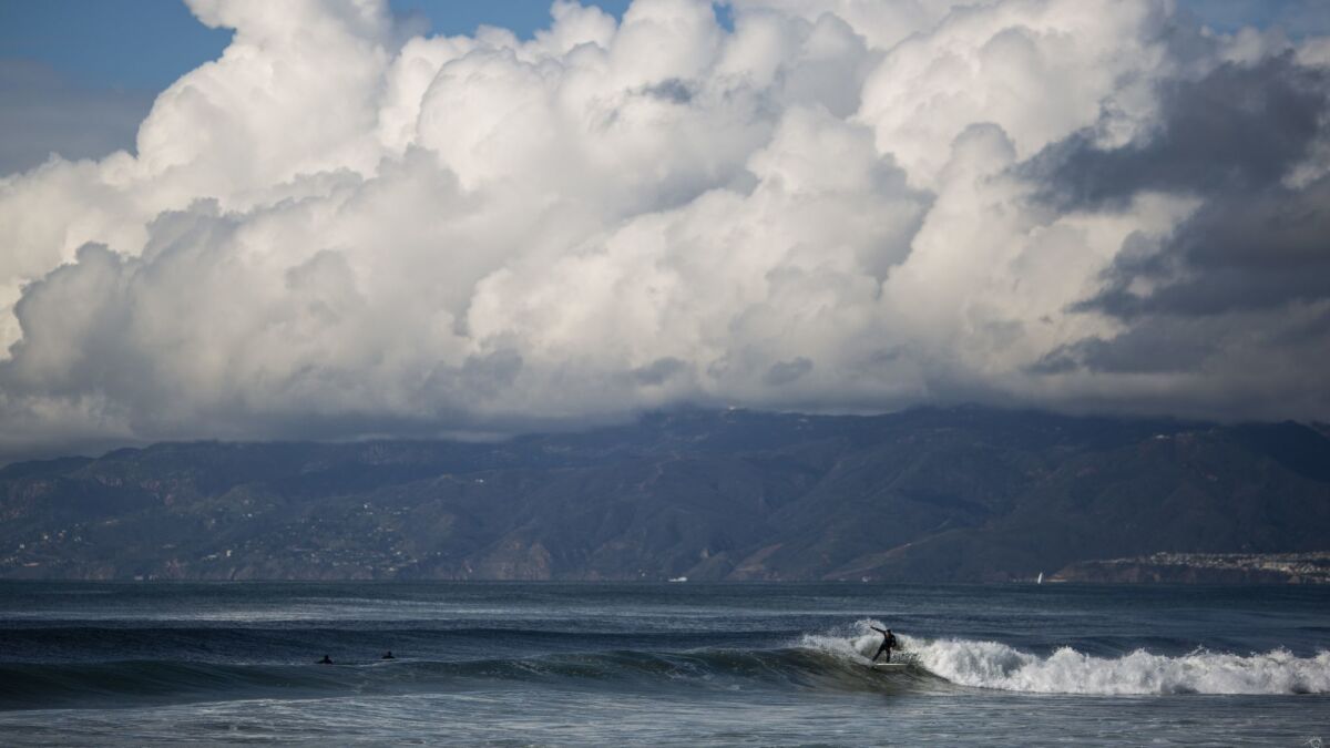 A surfer at Dockweiler State Beach on Saturday. Rain is in the forecast for most of the week in Southern California, raising the risk of debris flow, coastal flooding and high surf through Thursday.
