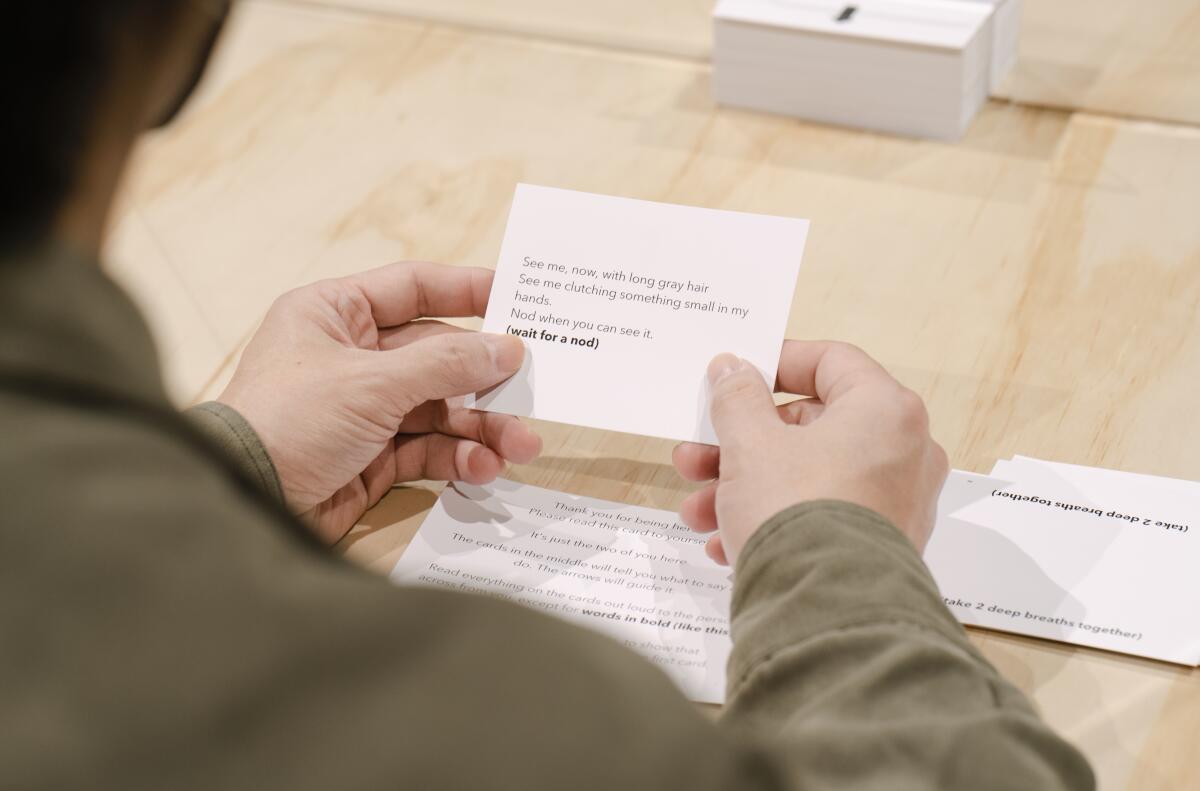 Two hands hold an index card with instructions for how to imagine a stranger sitting opposite you in "An Encounter." 