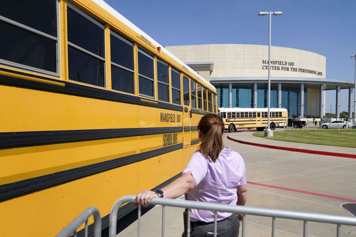 School busses depart past a law enforcement official after dropping off Timberview High School children at the Mansfield ISD Center For The Performing Arts, Wednesday, Oct. 6, 2021 in Mansfield, Texas, following a school shooting at Timberview in nearby Arlington. (AP Photo/Tony Gutierrez)