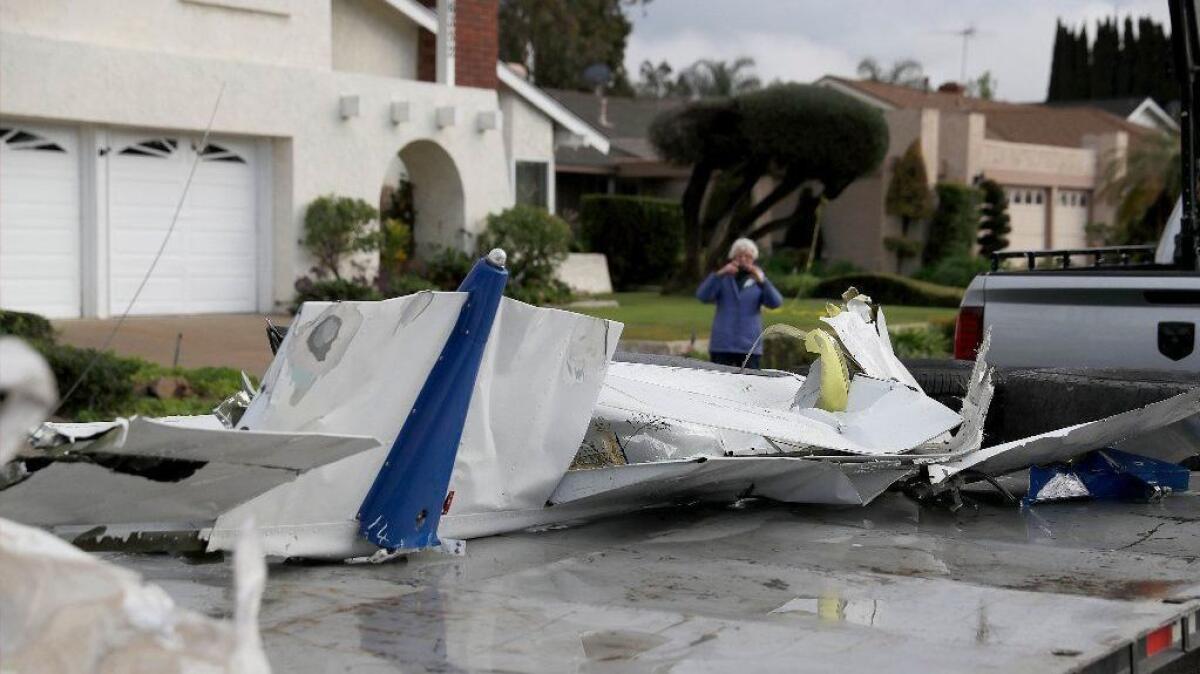 A woman takes a photo of airplane parts that landed on her property as workers remove wreckage after a crash of a Cessna after it crashed in Yorba Linda on Sunday, killing the pilot and four people inside a home.