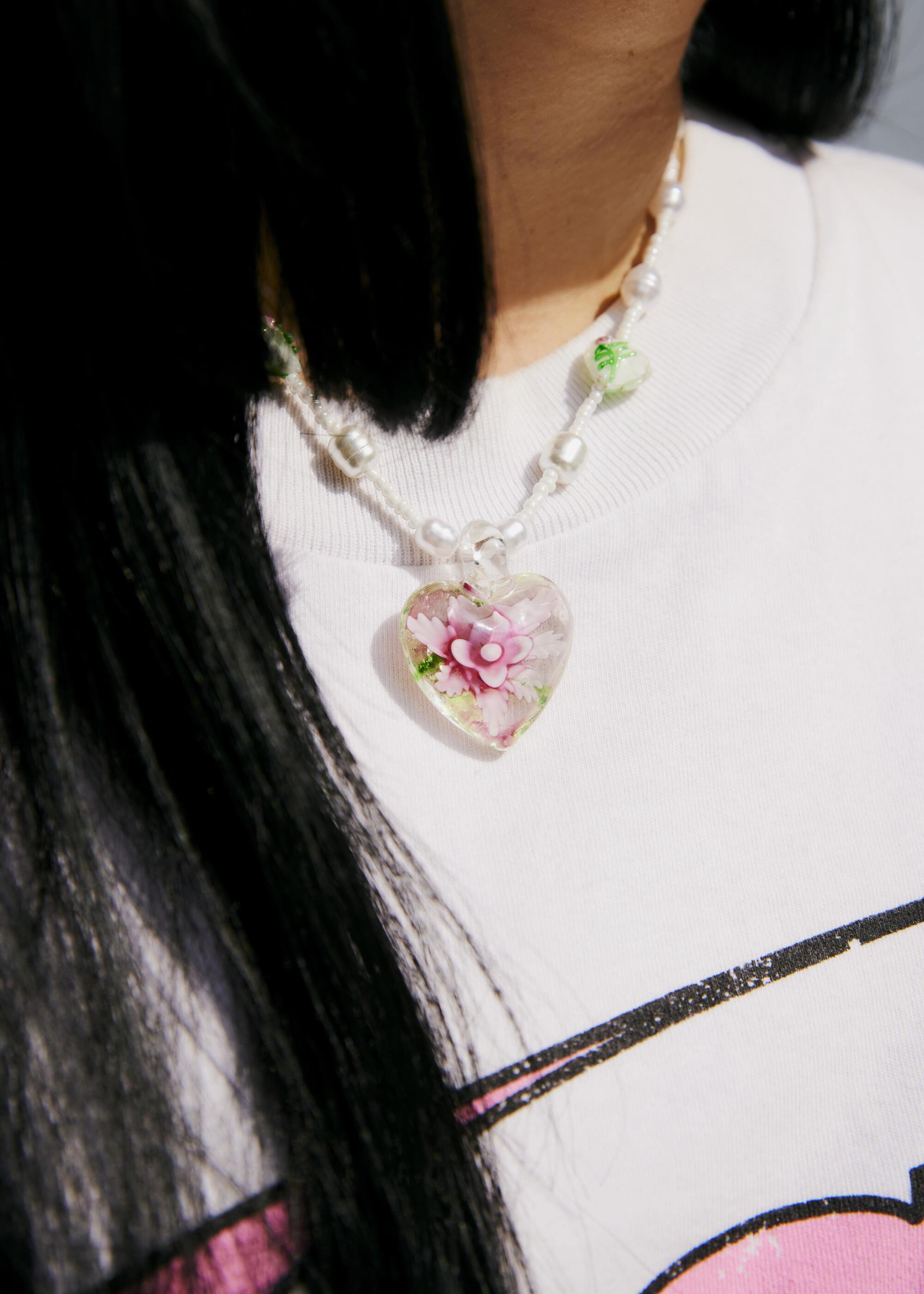 Détail d'un collier en forme de coeur sur un pull blanc.