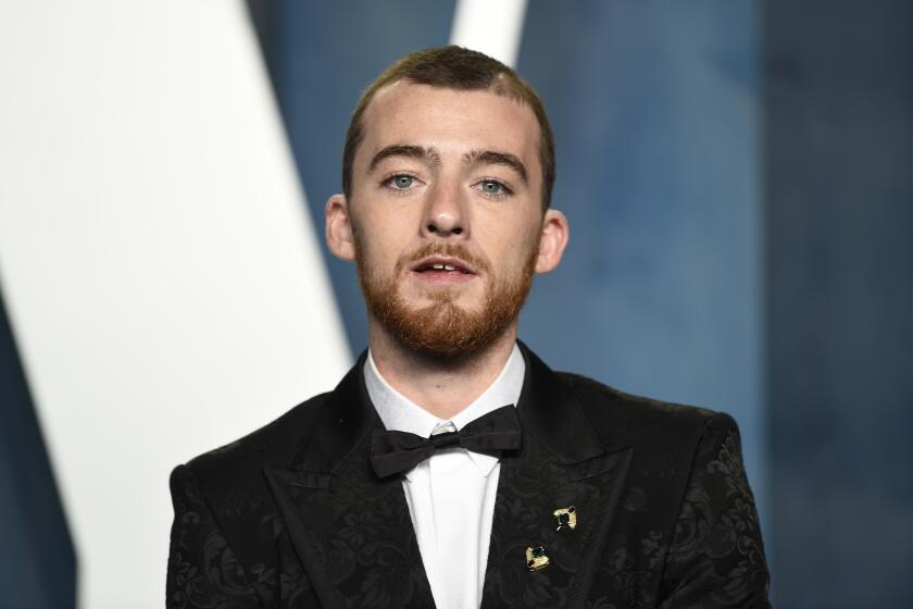 Angus Cloud in a tuxedo standing in front of a blue background