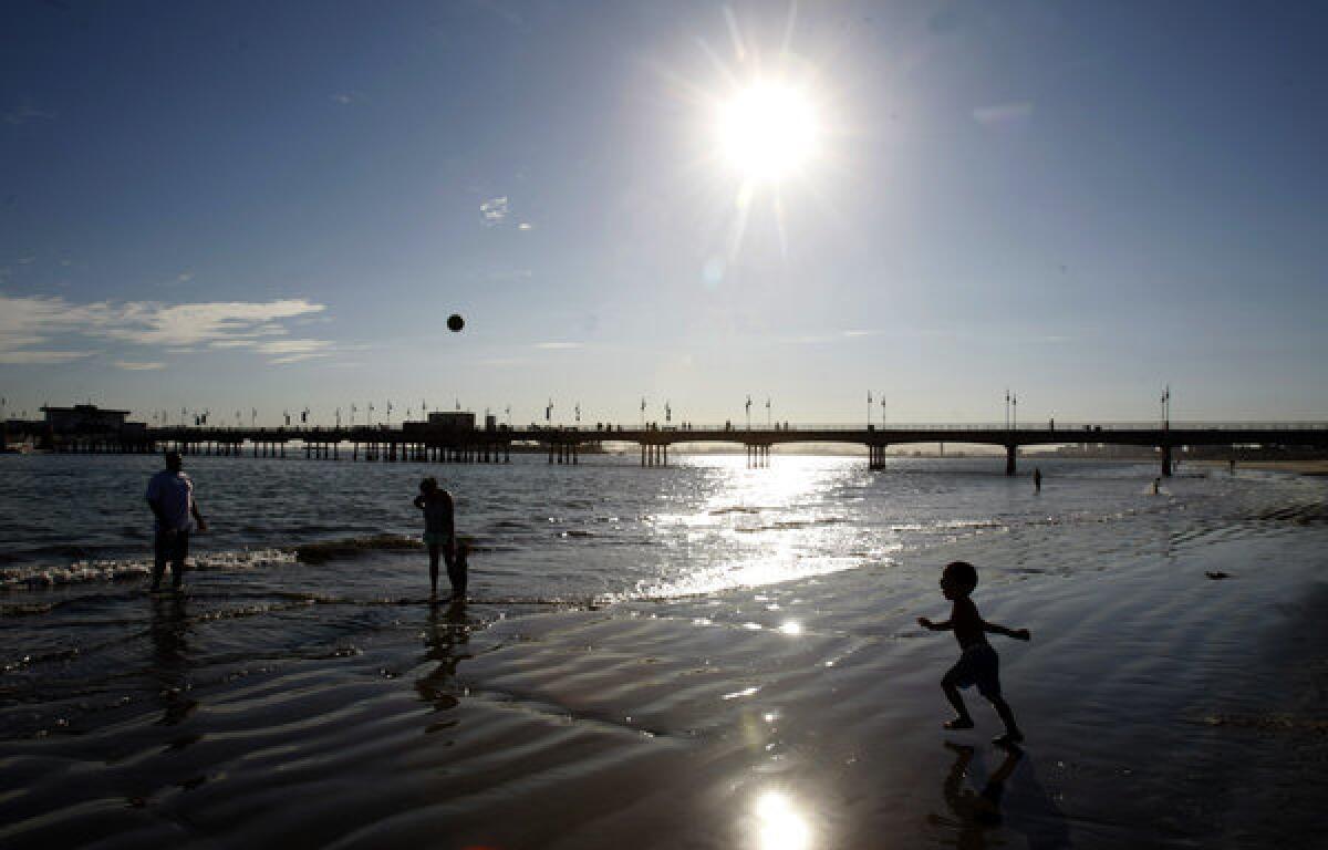 Jamie Jones, on the left, throws a ball to his son Jai in the Belmont Shore area of Long Beach. The Glendale family went to the beach to escape the heat.