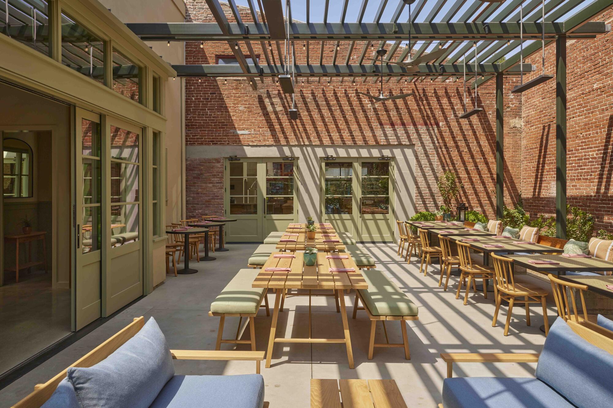 A view of a sunny dining patio features picnic tables under a steel trellis