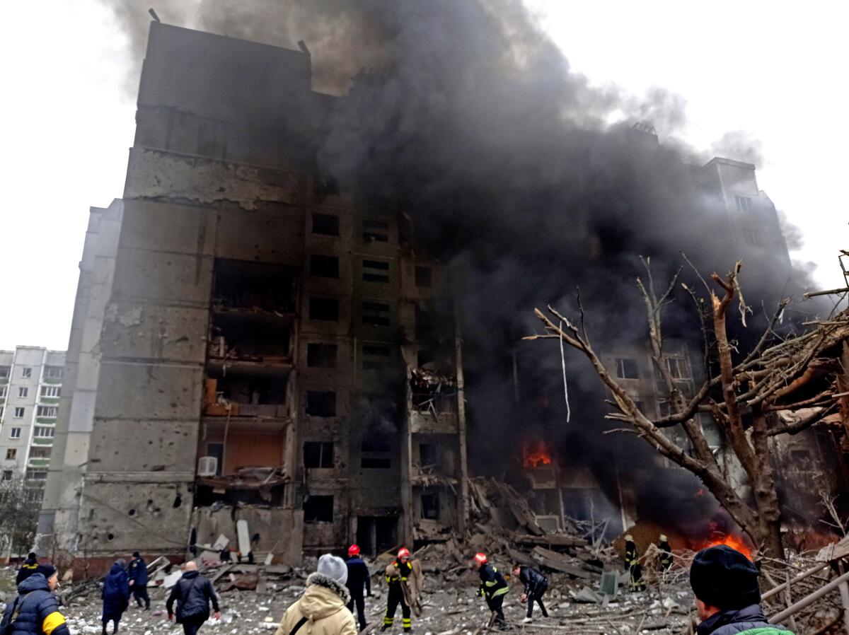 People are seen in front of a multistory building spewing smoke and flames