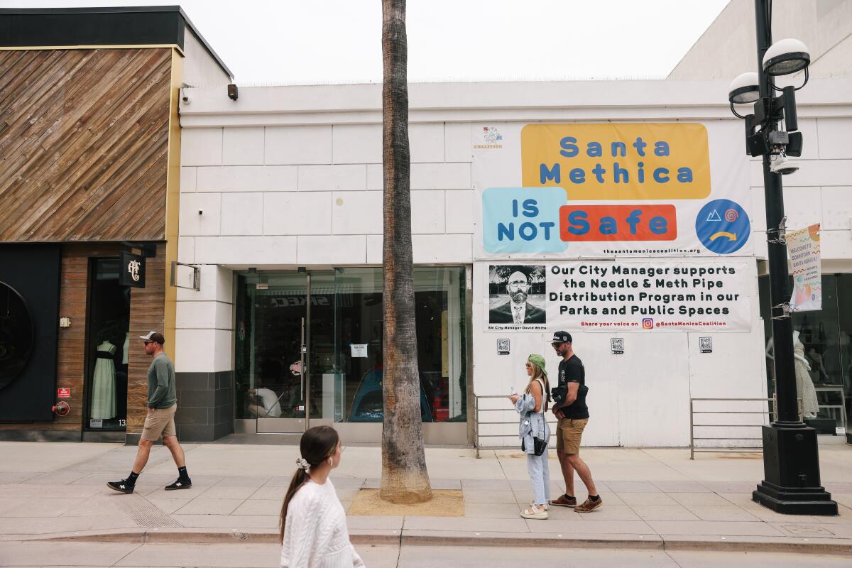 People walk past a "Santa Monica is not safe" sign.
