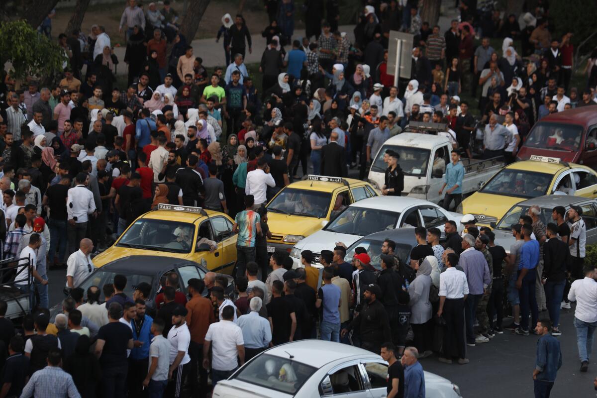 Dozens of Syrians wait at a bridge amid cars