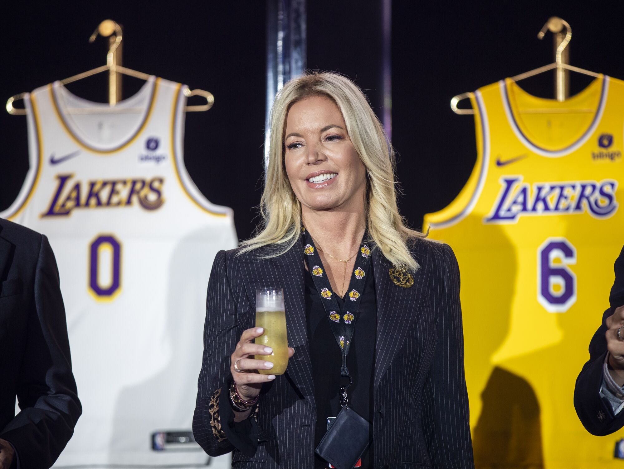 A woman toasts with a stemless flute while standing in front of two Lakers jerseys