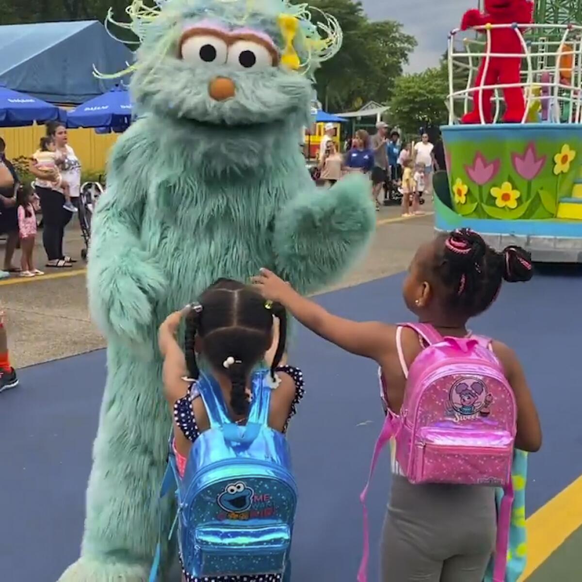 A person in a large, fluffy costume looks down at two little girls reaching out to them
