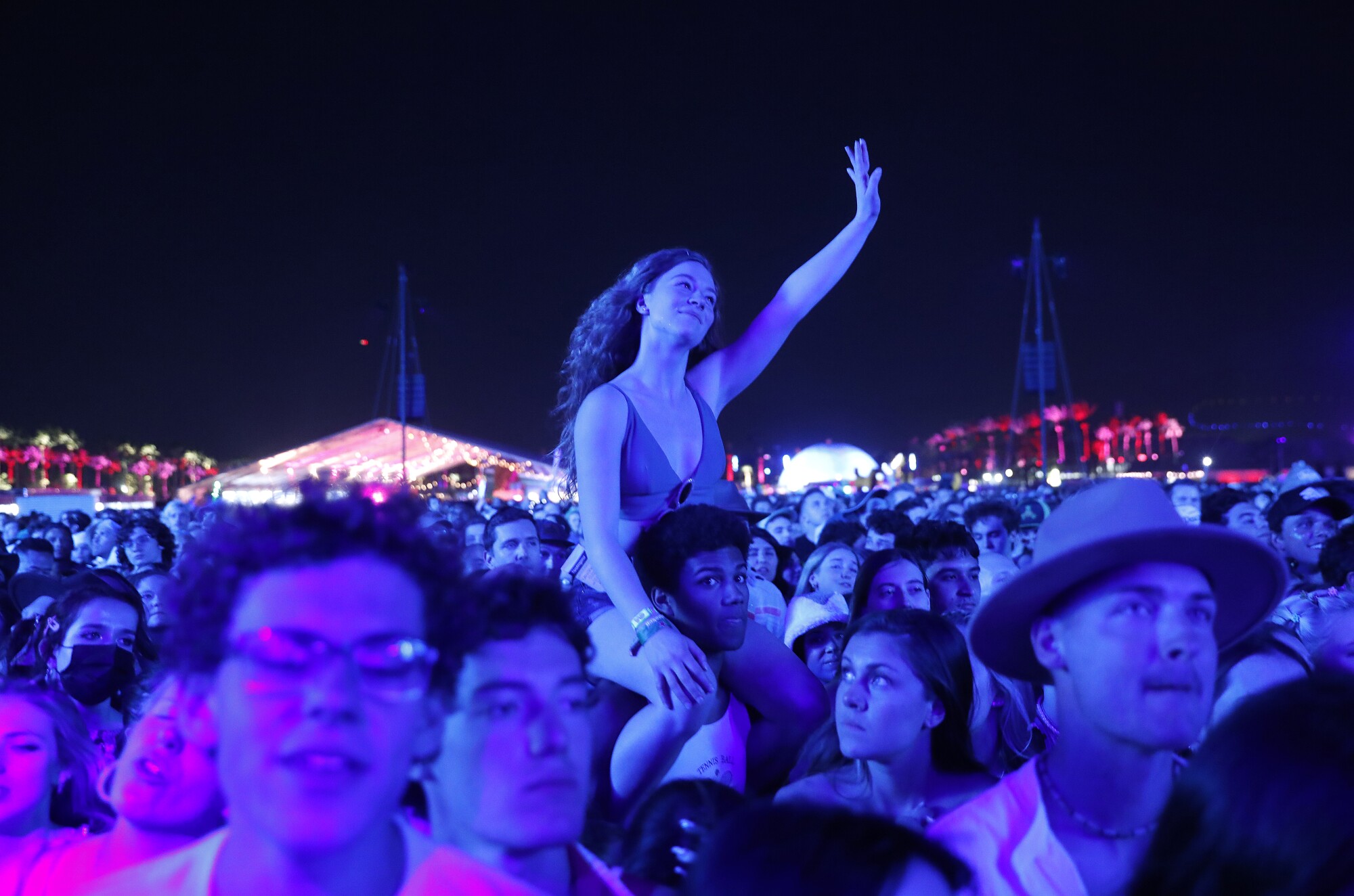 Fans in purple-tinted light watch a performance at night.