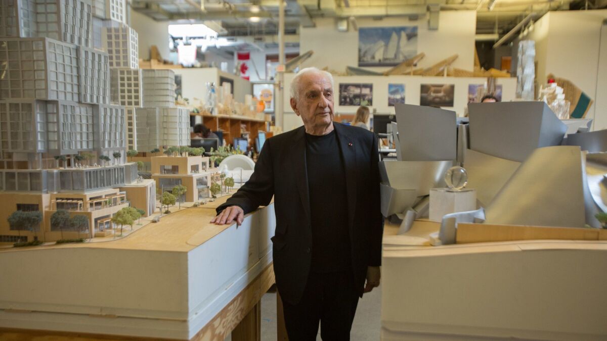 Frank Gehry in his Los Angeles office standing between models of the Grand development and Walt Disney Concert Hall.