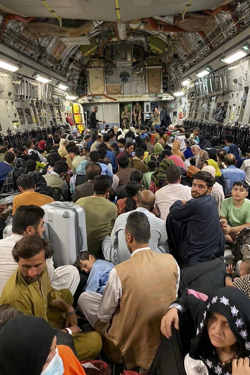 A crowd of Afghan people sit on the floor of a plane.