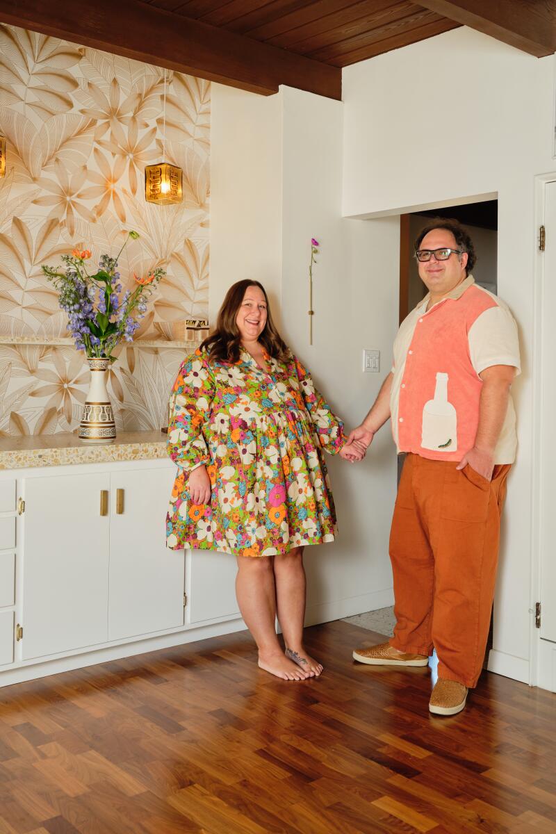 Jessica and Art Martinez hold hands and smile at the camera in front of their tiki bar.