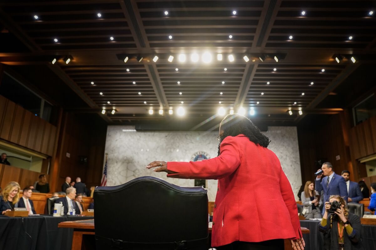  Judge Ketanji Brown Jackson pictured from behind as she prepares to sit under bright lights in a hearing room