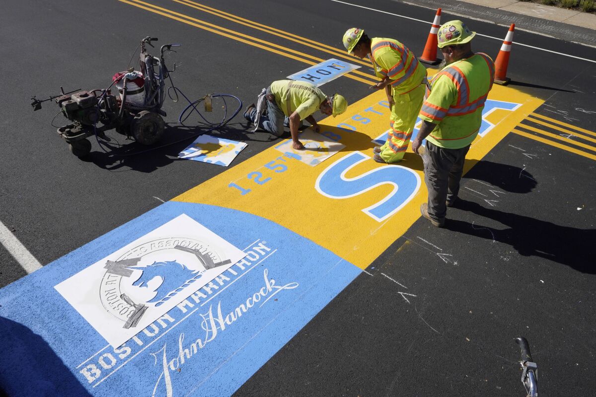 Painter Will Belezos, of Holbrook, Mass., left, uses a stencil, Wednesday, Oct 6, 2021, while working to complete the start line for the 125th edition of the Boston Marathon, in Hopkinton, Mass. The race is to be run on Monday, Oct. 11. (AP Photo/Steven Senne)