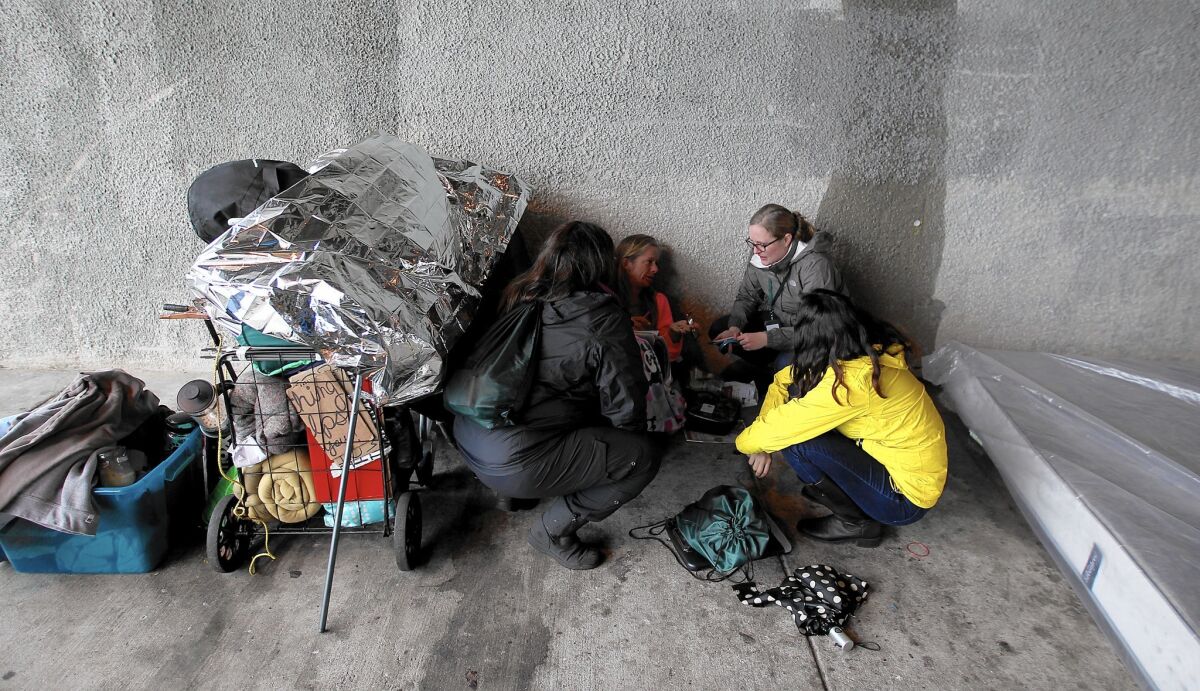 Outreach workers talk to a homeless woman named Sandy as she seeks shelter from the rain beneath the 405 Freeway in Venice.
