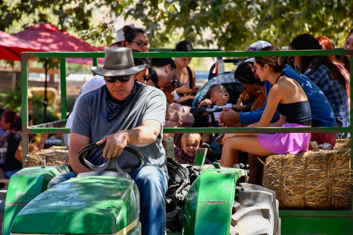 A person sits on a tractor as others sit on hay bales