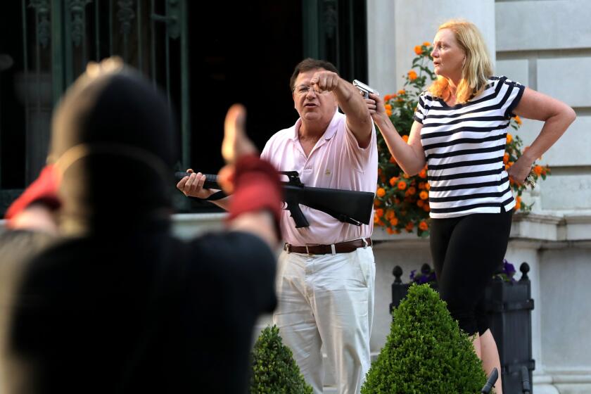 FILE - In this June 28, 2020 file photo, armed homeowners Mark and Patricia McCloskey, standing in front their house along Portland Place confront protesters marching to St. Louis Mayor Lyda Krewson's house in the Central West End of St. Louis. St. Louis’ top prosecutor told The Associated Press on Monday, July 20, 2020 that she is charging a white husband and wife with felony unlawful use of a weapon for displaying guns during a racial injustice protest outside their mansion. (Laurie Skrivan/St. Louis Post-Dispatch via AP File)