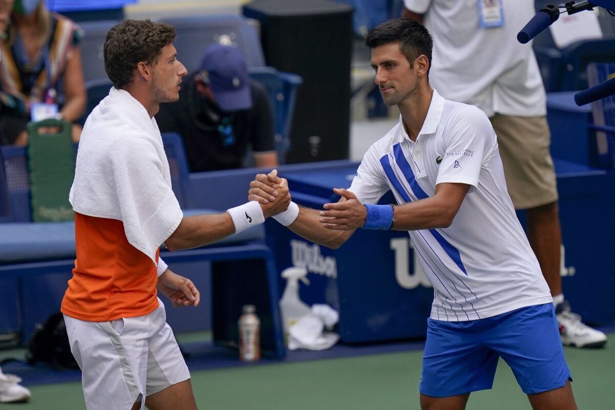 Novak Djokovic, of Serbia, shakes hands with Pablo Carreno Busta, of Spain, after defaulting the match during the fourth round of the US Open tennis championships, Sunday, Sept. 6, 2020, in New York. Djokovic inadvertently hit a line judge with a ball after hitting the ball in reaction to losing a point to Carreno Busta. (AP Photo/Seth Wenig)