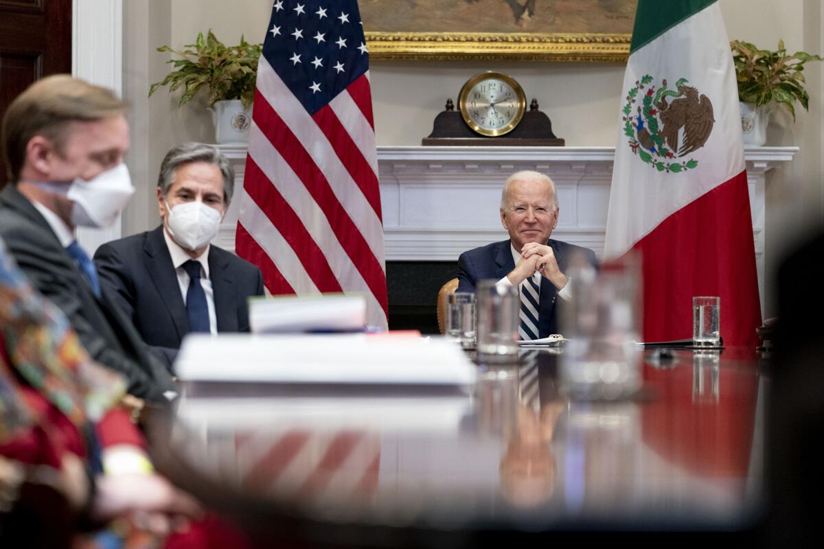 President Biden, Jake Sullivan and Antony J. Blinken meeting at a table, with the U.S. and Mexican flags in the background.