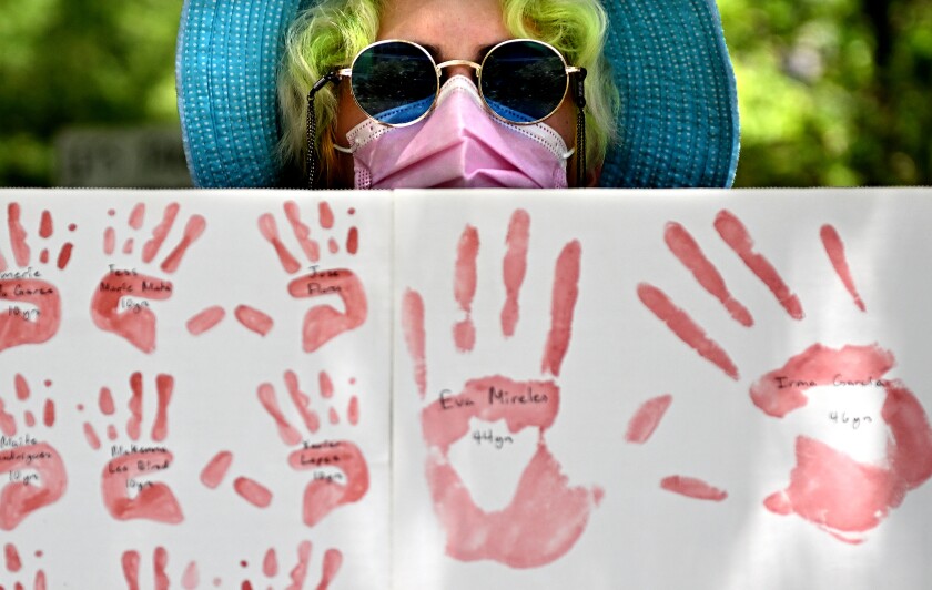 A person holds a poster with red handprints on it.
