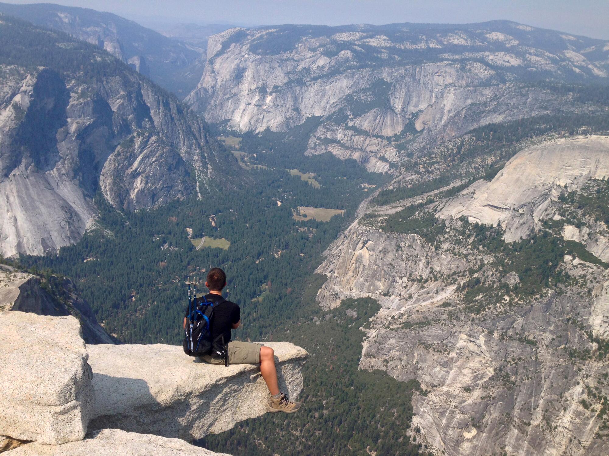 A hiker sits on a rock outcropping at the top of Yosemite's Half Dome.